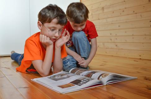 Dwóch kilkuletnich chłopców czyta książkę na podłodze w domu