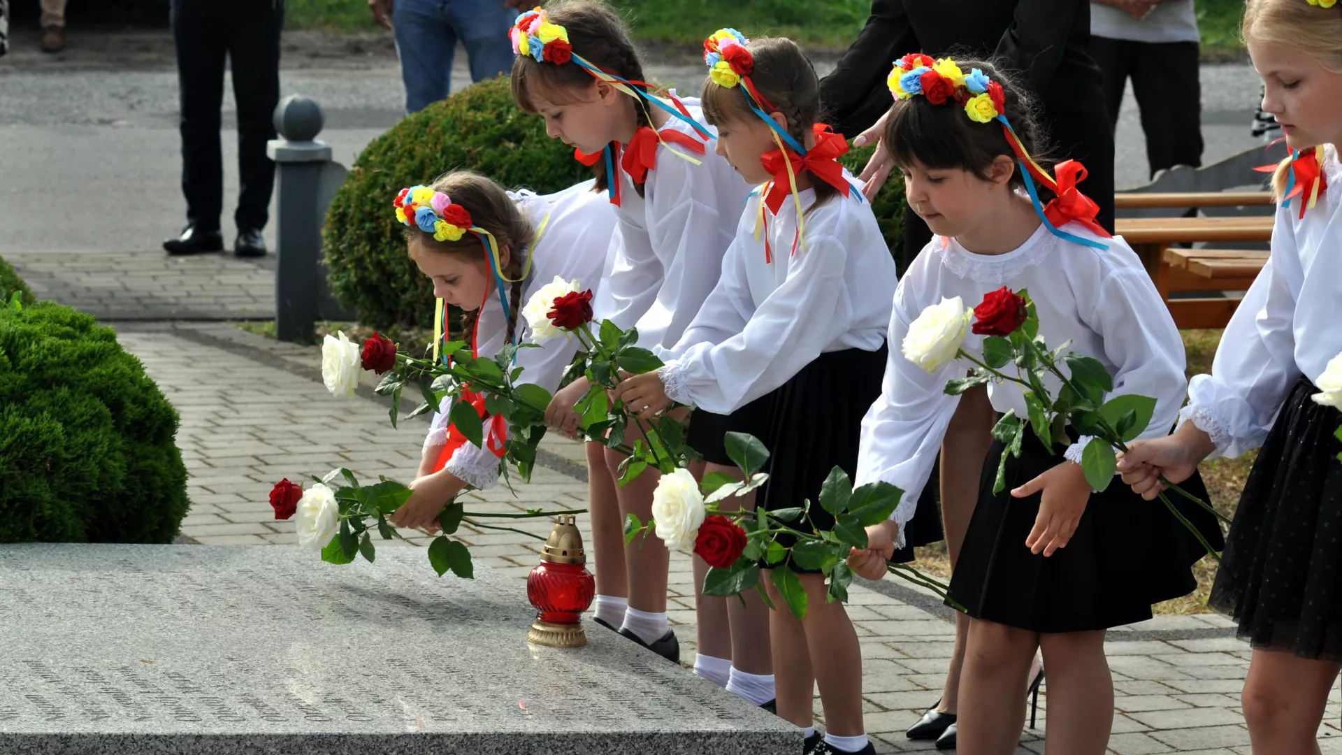 Dzieci składają kwiaty na tablicach z nazwiskami ofiar wojny.