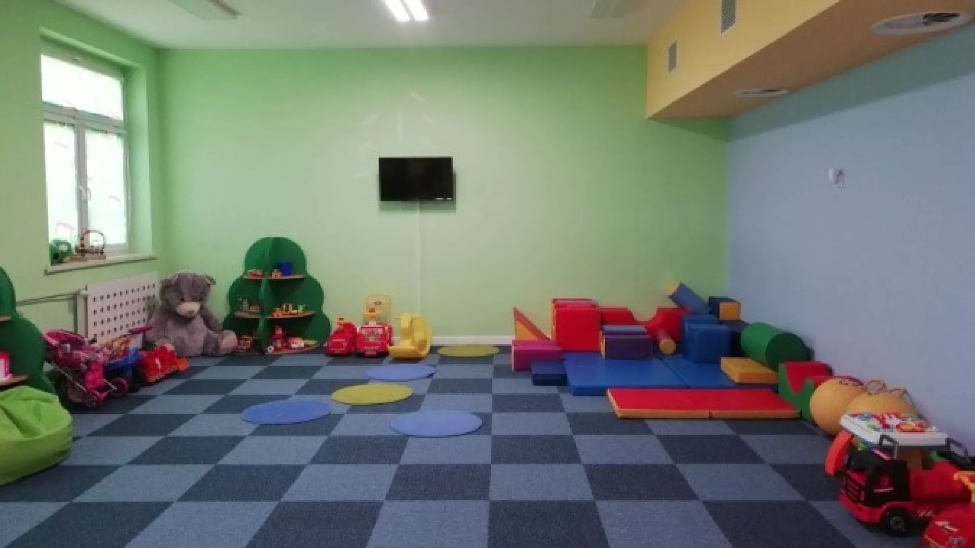 Duża sala z jadalnią, wyposażona w meble, zabawki i pomoce dydaktyczne odpowiednie dla dzieci do lat 3 wprowadzające je w świat zabawy i nauki