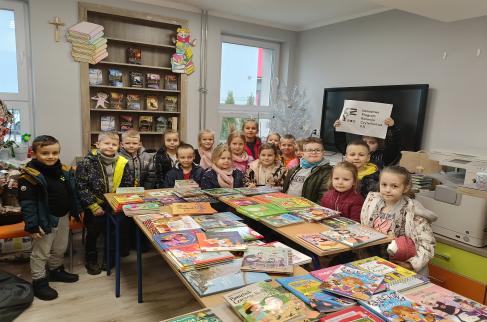 Grupa przedszkolaków podczas zajęć w bibliotece szkolnej z książkami nowo zakupionymi w ramach NPRCZ.