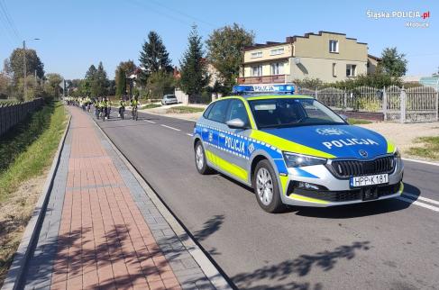 Radiowóz policyjny eskortuje grupę uczestników rajdu rowerowego, jadącą drogą powiatową w Lipiu.