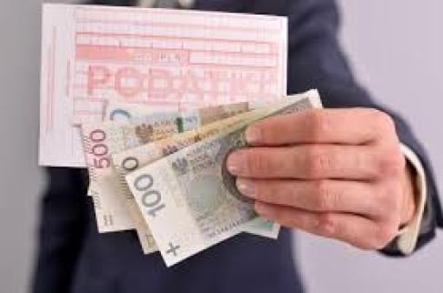 Ręka trzymająca blankiet przelewu z napisem podatki oraz banknoty o nominale sto, dwieście i pięćset złotych.